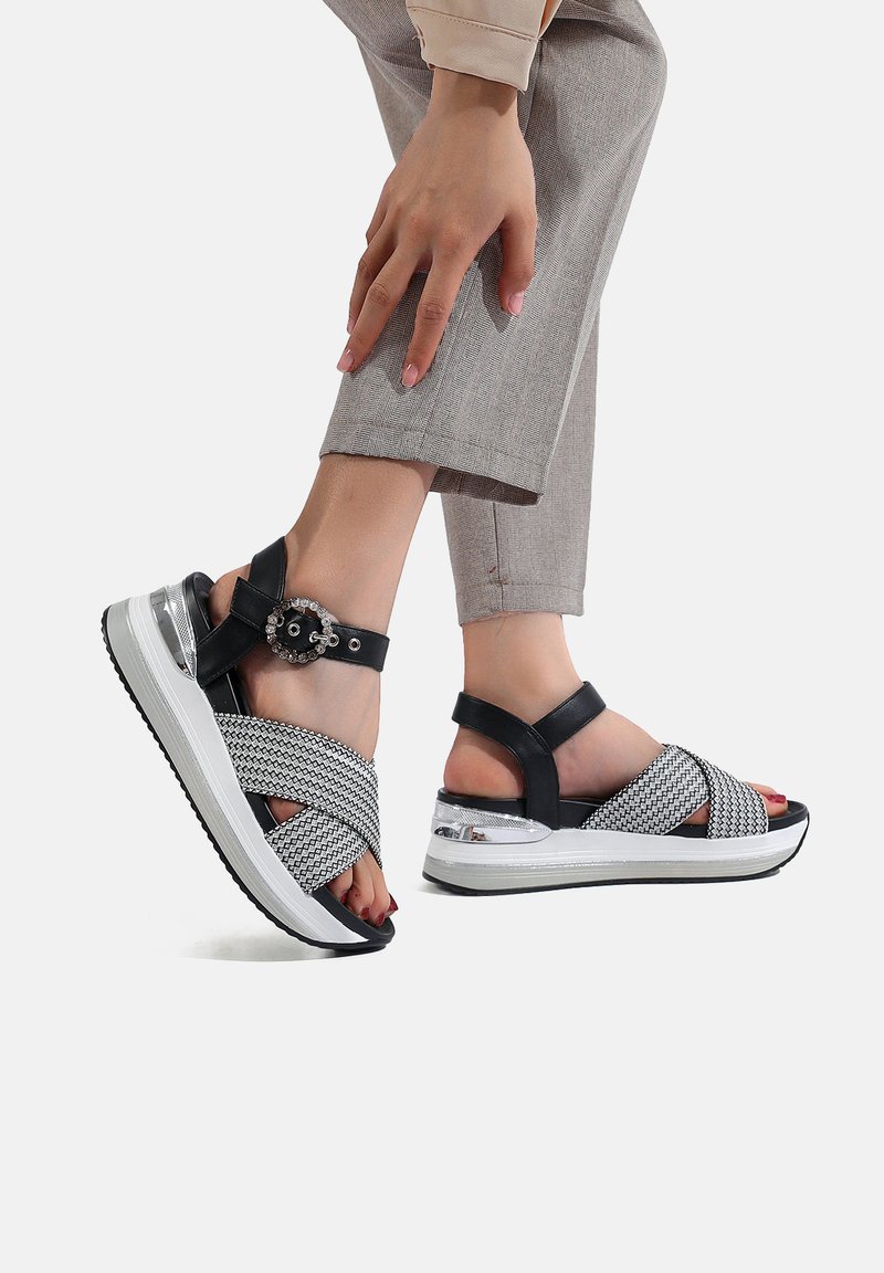 Sandali intrecciati in bianco e nero con una suola spessa bianca, dotati di una fibbia decorativa e un design a fasce incrociate; dettagli in pelle liscia.