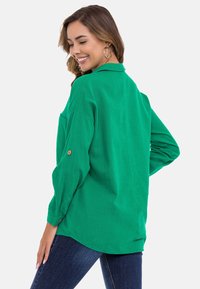 Losse groene blouse van geweven stof, met een puntkraag, opgerolde mouwen met knoopdetails en een ronde zoom.