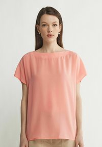 Løs pasform, kortærmet top i lys koralfarvet stof, med en glat, blød tekstur og en bred halsudskæring. Minimalistisk design, uden mønstre.