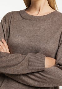 Brązowy sweter z dzianiny z okrągłym dekoltem i prążkowanymi mankietami. Charakteryzuje się teksturowanym, miękkim materiałem oraz luźnym krojem.