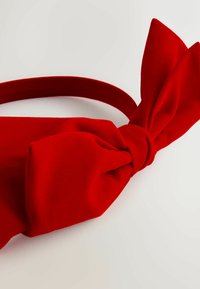 Rotes Stoffhaarband mit einem großen Schleifendetail, das eine glatte Textur und ein kreisförmiges Band aufweist. Die Schleife ist in der Mitte geknotet.