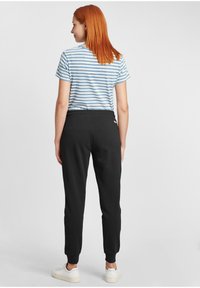 Zwarte joggers met elastische boorden en een tailleband, gecombineerd met een blauw-wit gestreept T-shirt. De achterkant van de outfit is zichtbaar.