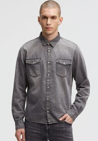 Graues Denim-Shirt mit langen Ärmeln, Knopfleiste, zwei Brusttaschen und Kontrastnähten. Weiche Textur, lässige Passform.