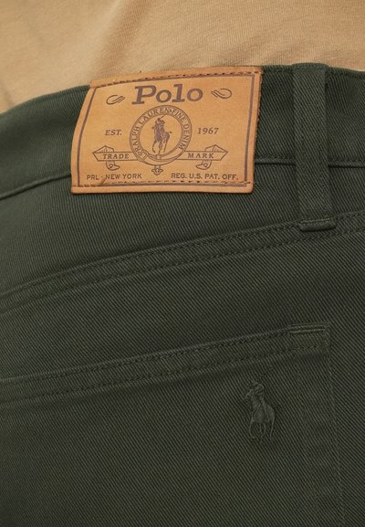 Temnozeleni denim hlače imajo svetlo rjavo usnjeno oznako s "Polo" blagovno znamko, logotip konja in kontrastno šivanje, ki prikazuje teksturirano tkanino.