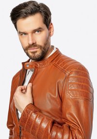 Braune Leder-Motorradjacke mit gesteppten Schulterdetails und hohem Kragen. Verfügt über einen Frontreißverschluss und ein tailliertes Design.
