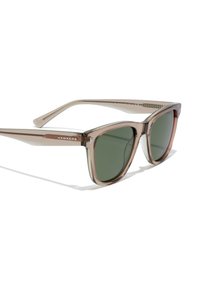 Ochelari de soare din plastic transparent brun cu lentile de culoare verde închis, formă unghiulară și detalii din metal pe braț, având numele brandului "Hawkers".