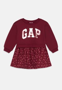 Maroon haljina s gornjim dijelom u stilu dukserice sa "GAP" logom u metalik srebrnoj boji i suknjom s cvjetnim uzorkom. Dugi rukavi i rebrasti manšeti.