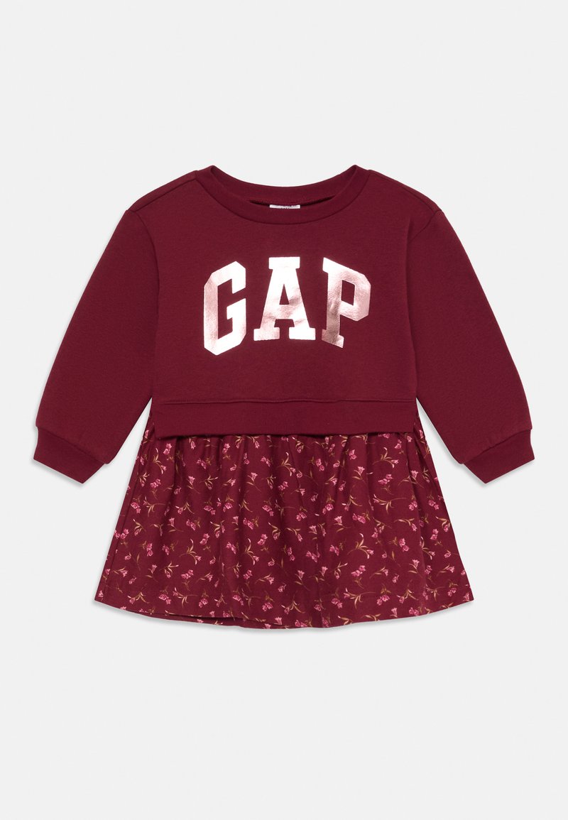 Maroon haljina s gornjim dijelom u stilu dukserice sa "GAP" logom u metalik srebrnoj boji i suknjom s cvjetnim uzorkom. Dugi rukavi i rebrasti manšeti.