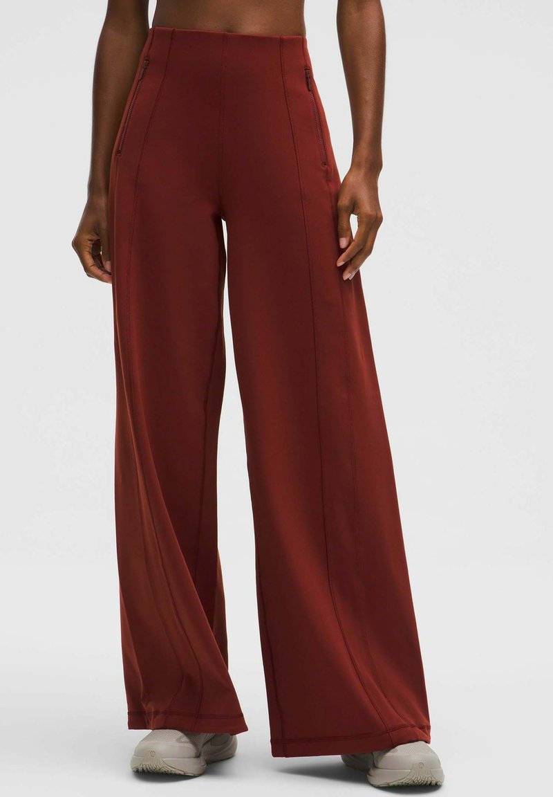 Bőszárú nadrág mély rozsdabarna színben, puha anyagból készült. Oldalsó zsebekkel és varrás részletekkel rendelkezik, világosszürke cipővel párosítva.