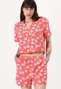 Rød blomstertrykt kortermet skjorte med knapper og matchende shorts. Lett stoff med hvite blomster mønstre og elastisk midjebånd.