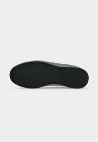 Semelle en caoutchouc noire d'une chaussure à profil bas avec des lignes de bande de roulement horizontales et le logo "BOSS" sur la zone du médio-pied.