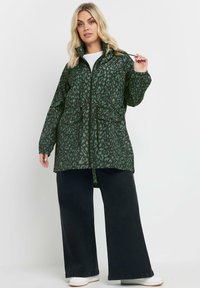 Grön leopardmönstrad jacka med dragkedja fram, elastiska ärmmuddar, justerbar midja och två framfickor, parat med vida svarta jeans.