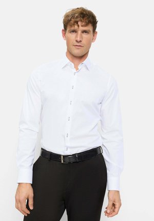 Man wearing a white long-sleeve dress shirt with patterned buttons tucked into black pants with a black leather belt.