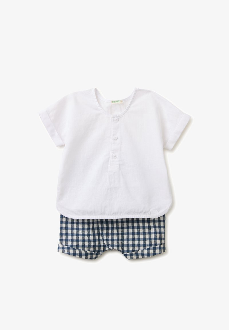 Chemise blanche bébé à manches courtes avec trois boutons, associée à un short à carreaux bleu et blanc sur fond blanc.