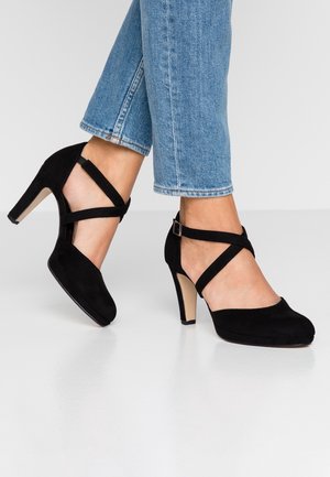 Schwarze Wildleder-High Heels mit einem Kreuzband-Design. Runde Zehenpartie, geschwungene Silhouette und ein Mittelhoher Absatz. Strukturiertes Material.