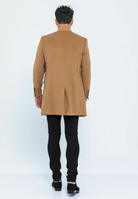 Brauner Woll-Mix-Mantel mit maßgeschneidertem Design und einem Schlitz hinten, kombiniert mit schwarzen Skinny Jeans und dunklen Schuhen.