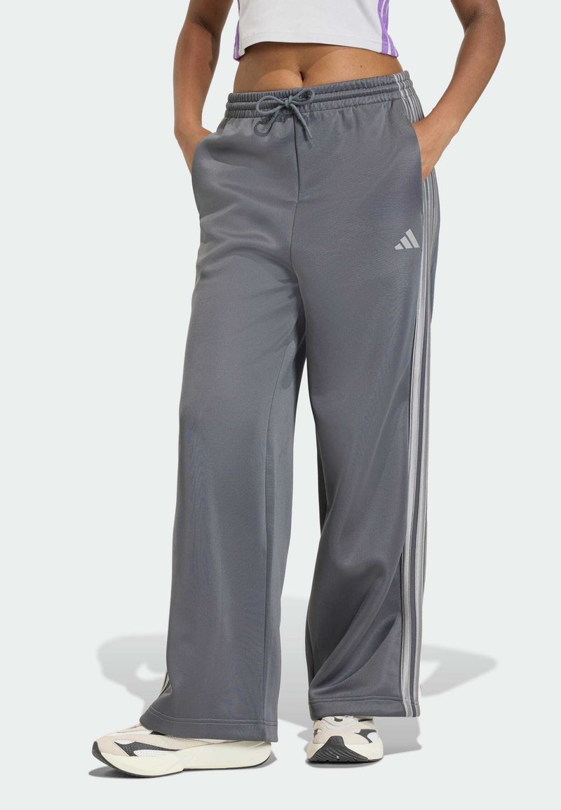Šedé športové nohavice s voľným strihom, elastickým pásom a šnúrkou. Sú vybavené tromi bielymi pruhmi po stranách. Vyrobené z hladkého materiálu.