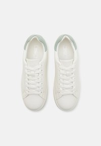 Fehér sneaker, textúrált mentazöld kiegészítőkkel a sarkon, kerek orral és fűzőkkel, sima felülettel és diszkrét logóval a nyelvén.