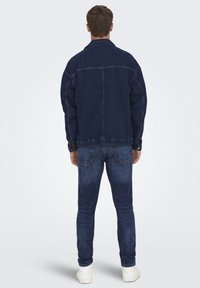 Jachetă din denim albastru închis cu o croială lejeră, cusături vizibile și guler clasic, asortată cu blugi albastre închise și adidași albi.