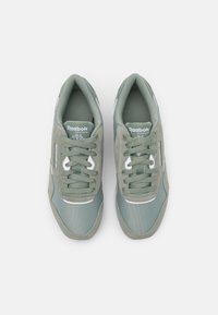 Un par de zapatillas Reebok Classic de color gris-verde con cordones, con la marca visible en las lenguas y los laterales, mostradas desde una vista superior sobre un fondo blanco.