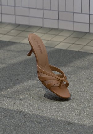 Sandale à talon en cuir marron Steve Madden avec fines lanières et bout carré, positionnée verticalement sur l'asphalte près d'un mur carrelé.