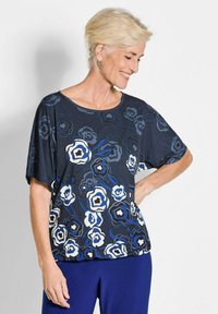 Korte mouwen marineblauw shirt met bloemenpatroon in blauw, wit en zwart. Zachte stof, ronde halslijn, losse pasvorm en zichtbare stiksels.