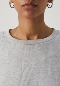 Camiseta de algodón gris claro con cuello redondo, que presenta una textura suave y mínimas arrugas. Se muestra un primer plano del escote y la piel.