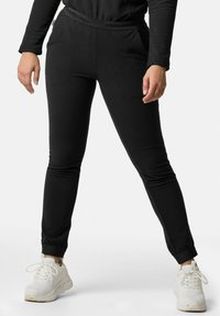 Schwarze tapered Jogginghosen aus strukturiertem Stoff, mit elastischem Bund und seitlichen Taschen, kombiniert mit weißen Sportschuhen.