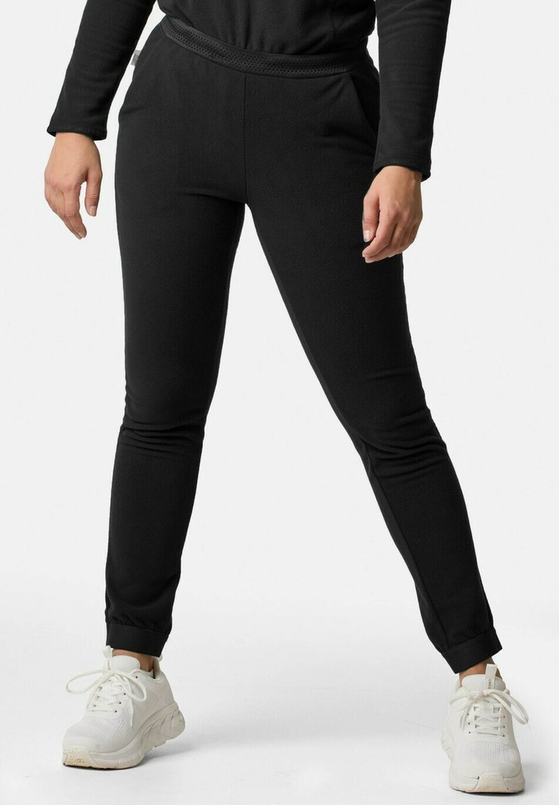 Schwarze tapered Jogginghosen aus strukturiertem Stoff, mit elastischem Bund und seitlichen Taschen, kombiniert mit weißen Sportschuhen.