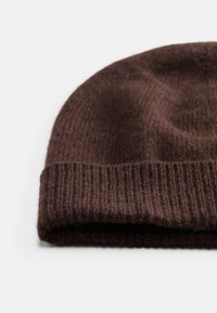 Bonnet tricoté brun avec une texture côtelée et un revers replié. Fabriqué en laine douce, il présente un motif de surface légèrement irrégulier.