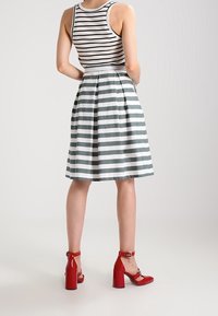 Randig, ärmlös topp med grå och vita ränder, i kombination med en knäd-length, utsvängd kjol i matchande ränder. Bärs med röda klackskor.