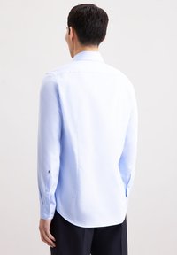 Camicia a maniche lunghe di colore azzurro chiaro realizzata in tessuto morbido, con colletto classico e polsini abbottonati. Orlo curvo e vestibilità su misura.