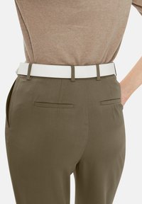 Olijfgroene broek met een gladde textuur, voorzien van een witte leren riem en twee achterzakken. Subtiele plooien bij de taille.