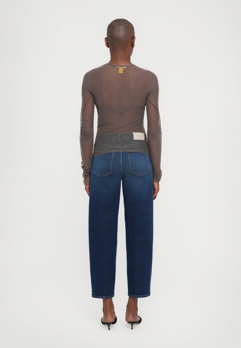 Gennemsigtig, langærmet top i brunt stof med strømlinet syning; parret med højtaljede blå jeans og sorte hæle-sandaler.