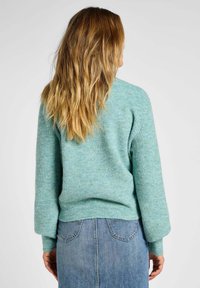 Maglione azzurro chiaro con lavorazione a maglia texturizzata, spalle calate e maniche lunghe. Indossato con una gonna di denim, che mostra una silhouette rilassata.