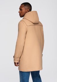 Beige plášť s kapucí a přiléhavým střihem, který se vyznačuje hladkou texturou, knoflíkovými manžetami a čistým, minimalistickým designem.