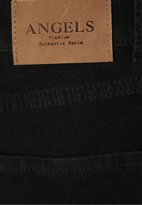Zwarte denimstof met een gestikte naad. Een rechthoekig bruin leren label met de tekst "ANGELS Premium Authentic Denim" in zwarte letters.