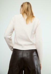 Maglione in lana rosa chiaro con orlo e polsini a coste, abbinato a pantaloni in pelle marrone a vita alta con tasche posteriori.