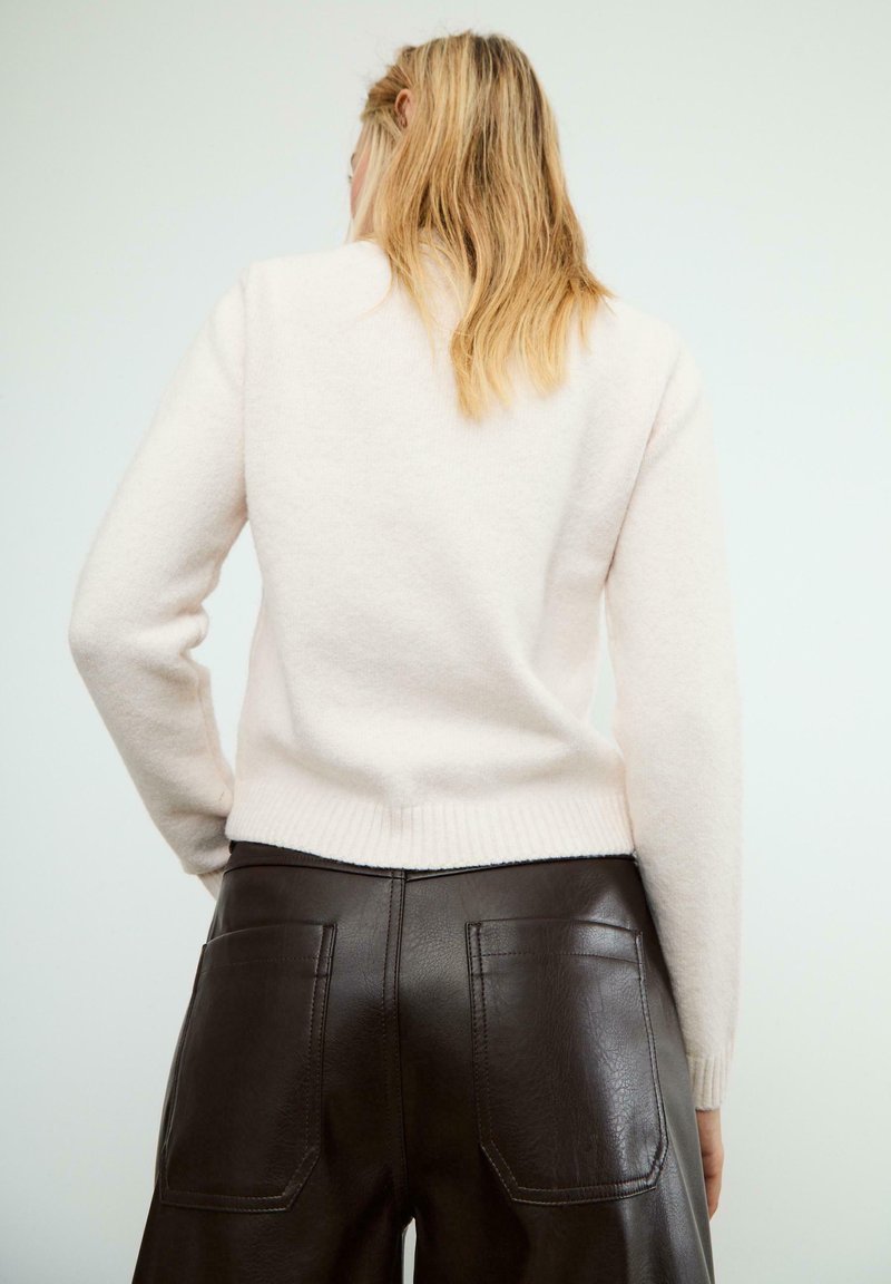 Maglione in lana rosa chiaro con orlo e polsini a coste, abbinato a pantaloni in pelle marrone a vita alta con tasche posteriori.