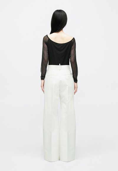 Zwarte doorschijnende top met lange mouwen en een off-shoulder ontwerp, gecombineerd met witte, wijde broek met achterzakken en een gladde textuur.
