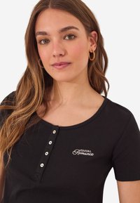 Zwarte geribbelde T-shirt met een ronde hals, korte mouwen, knopen aan de voorkant en witte borduursel met "Casual Romance" op de borst.