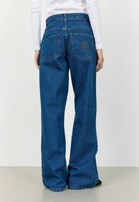 Jeans din denim albastru cu picioare largi au o talie înaltă, buzunare spate proeminente și detalii subtile de cusătura. Materialul are o textură netedă.