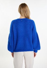 Maglione lavorato a maglia blu reale con texture a coste, maniche a sbuffo e scollatura rotonda. Presenta un piccolo etichetta con logo sul retro.