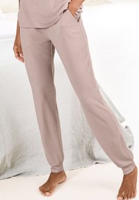 Light brown ribbed lounge pants with a relaxed fit, featuring side pockets and elastic cuffs, worn with a matching loose top.