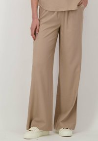 Beige wijd uitlopende broek van lichtgewicht stof, met een ontspannen pasvorm, elastische tailleband en zijzakken. Gepaarde met witte sneakers.