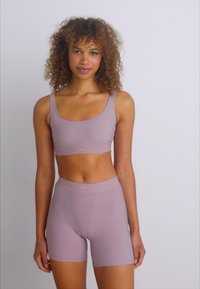 Reggiseno sportivo viola chiaro e pantaloni shorts a vita alta realizzati in un tessuto liscio ed elastico, con un design aderente e cuciture minime.