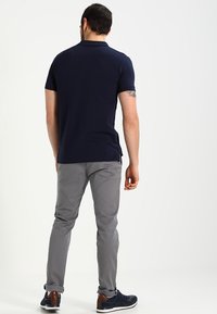 Polo-shirt navy à manches courtes, coupe slim, porté avec un pantalon gris clair et des sneakers noirs. Comprend des fentes sur les côtés et un col.
