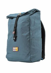 Mochila de tela en color teal, con tapa plegable y correa negra, detalles en marrón, bolsillo lateral y respaldo acolchado. Logo de Discovery en la parte frontal.
