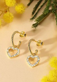 Guldpläterade hoopörhängen med en vriden design, prydda med hängande hjärtformer dekorerade med klara rhinestones. Texturerad yta och öppen mitt.