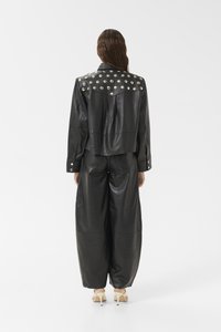 Zwart leren cropped jack met zilveren studs op de schouders, gecombineerd met wijde zwarte leren broeken. Gladde textuur, getailleerd ontwerp.
